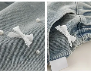 Dettaglio di pantaloncini di denim per bambina con fiocchi di maglia e perline bianche