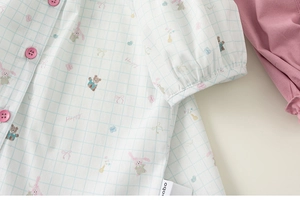 Detail of baby girl doll shirt featuring cartoon bear prints and pink buttons on plaid fabric