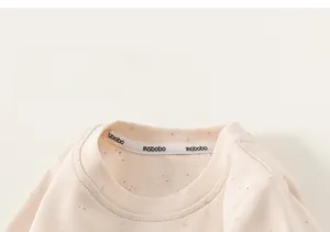 Détail d'un t-shirt doux pour bébé crème avec des mouchetures colorées et un col rond confort