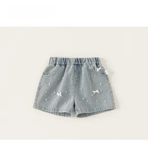 Dettaglio di pantaloncini di jeans celeste con eleganti perle bianche e fiocchi