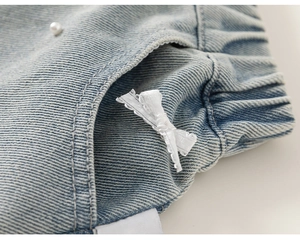 Dettaglio di pantaloncini in denim azzurro da bambina con fiocco in pizzo e perla