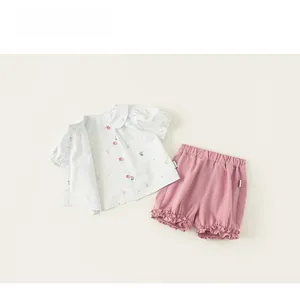 Flat lay of girl's summer outfit with floral doll collar shirt and pink ruffled shorts