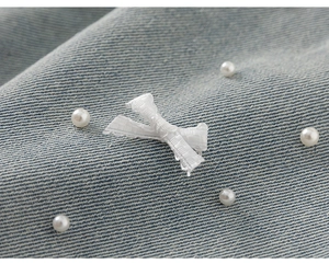 Dettaglio di pantaloncini di jeans celeste con fiocco in tessuto e perle bianche