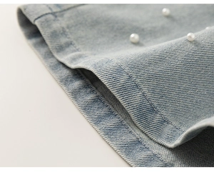 Dettaglio del tessuto denim azzurro con eleganti decorazioni di perline bianche