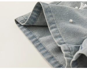 Dettaglio di pantaloncini in denim azzurro con perle decorative e cuciture rinforzate
