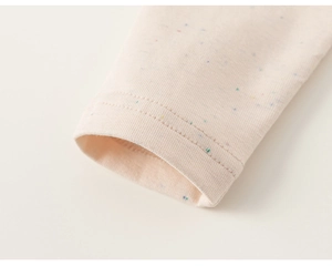Détail de la manche d'un t-shirt bébé en maille beige avec points colorés confettis