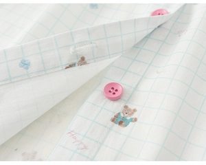 Macro shot of cotton baby shirt with light blue grid, bear patterns, and pink resin buttons