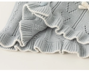 Detail der hellblauen Strickjacke mit Lochmuster und weißer Schleifenverzierung