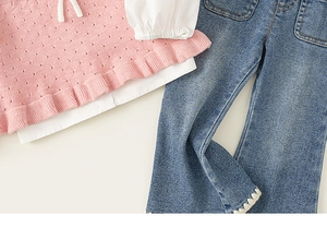 Detail of pink knit top with ruffled cuffs and blue denim flare pants with lace trim