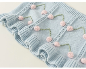Detail of light blue knit vest featuring pink cherry embroidery and scalloped ruffle hem