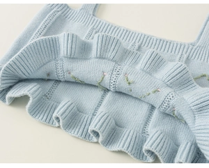 Detail of blue knitted vest featuring floral embroidery and tiered ruffle hemline