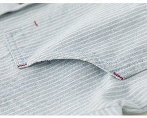 Close-up of light blue striped cotton fabric with red reinforced stitching on the pocket