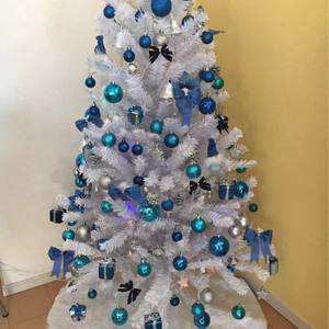White Christmas tree decorated with blue and silver ornaments on a white faux fur tree skirt