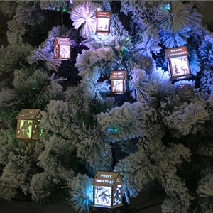 Lighted wooden Christmas house ornament with LED lights hanging on a snowy tree