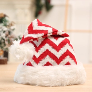 Knitted red and white striped Christmas hat with plush pompom on wooden surface