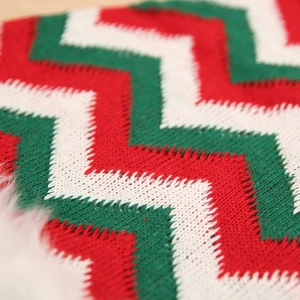 Close-up of red and green striped knit fabric with white faux fur trim on wood