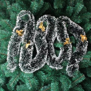 Green and white Christmas tinsel garland with gold bows on evergreen tree branches