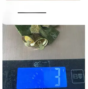 Close-up of 3g Christmas burlap bow with bells showing weight on a digital scale