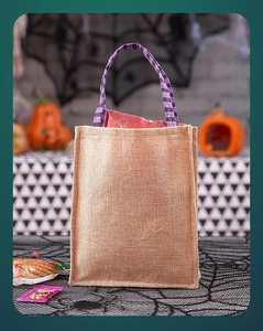 Detail of burlap Halloween gift bag with purple and black striped handles on festive table