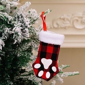 Red and black plaid Christmas stocking with white paw print hanging on a snowy pine tree