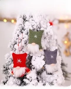 Close-up of knit Christmas gnomes with snowflake embroidery hanging on a snowy tree