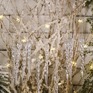 Macro shot of twisted acrylic Christmas icicle ornaments hanging on snowy pine branches