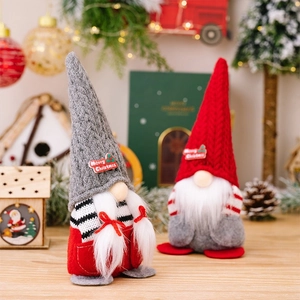 Pair of red and grey knitted Christmas gnomes with Merry Christmas signs on wooden desk