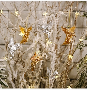 Golden and silver angel figurines hanging on a snow-decorated tree with warm lights