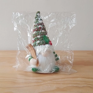 Detail of Christmas gnome plush with knitted cap and wooden ornament in clear packaging