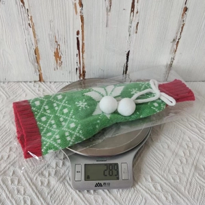 Detail of Christmas knitted wine bottle cover with snowflakes and white plush pom-poms