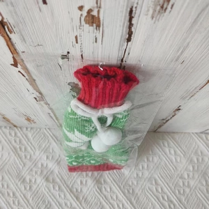 Close-up of knitted Christmas wine bottle cover in red and green with white pompoms