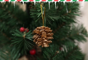 Golden pine cone ornament with hanging string displayed on a lush Christmas tree branch