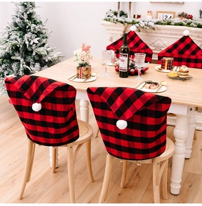Detail of red and black buffalo plaid Christmas hat chair covers with white plush pompoms