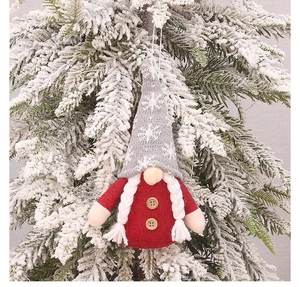 Detail of Christmas gnome ornament with red felt body and grey snowflake hat on a pine branch