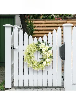 Detail of white rose wreath with green leaves hanging on a white wooden garden fence
