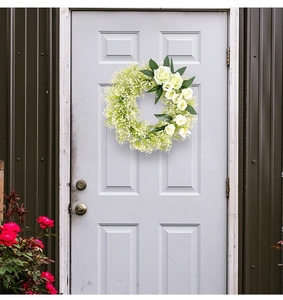 Close-up of white artificial rose wreath on a light grey door for wedding home decor