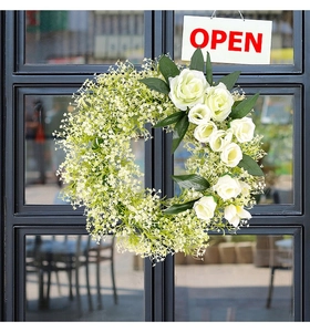 Close-up of white rose wreath with green leaves hanging on glass door for decor