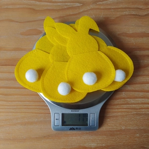 Detailed view of yellow bunny felt cutlery holders with white pom-pom tails for Easter table