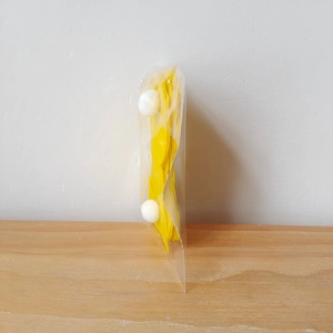 Detail of yellow Easter cutlery holder with white pompom tail in clear packaging