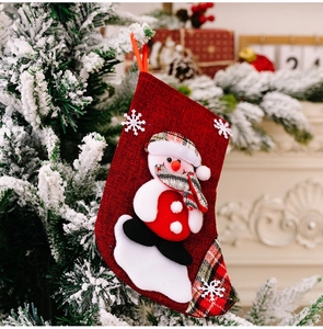 Close-up of red linen Christmas stocking with 3D snowman hanging on a snowy branch