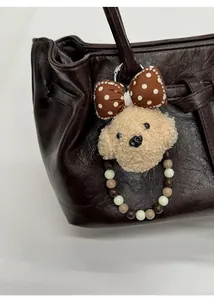 Close-up of a cute beige teddy bear plush charm with a polka dot bow on a brown leather bag