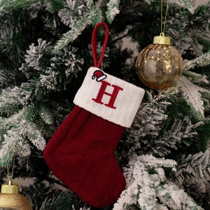 Close-up of red knitted Christmas stocking with white cuff and embroidered letter H