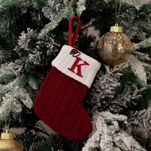 Detail of red cable-knit Christmas stocking with embroidered letter K on a snowy tree
