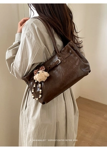 Close-up of retro brown leather tote with plush bear pendant and beaded charm detail