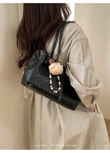 Detail view of black faux leather underarm bag with plush charm and beaded strap decor