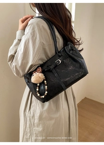 Close-up of retro black tote bag with glossy texture and animal plush charm on model