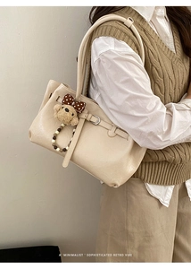 Detail of cream shoulder bag with plush bear charm and beaded strap on a knitted vest