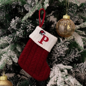 Close-up of a red knitted Christmas stocking with letter P hanging on a snowy tree