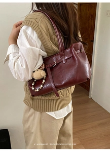 Detail of burgundy leather tote bag featuring a retro buckle and cute bear charm accent