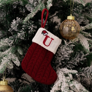 Detail of red knitted Christmas stocking with white cuff and letter U on a festive tree